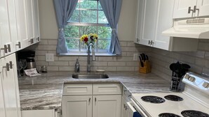 A modern kitchen with white cabinets, a built-in oven, a sink, and a window with blue curtains.