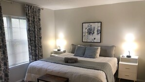 A bedroom with a bed, bedside tables, a nightstand, a bench, and a window with curtains.