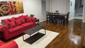 A living room with a red sofa, a coffee table, and a dining area with a table and chairs.