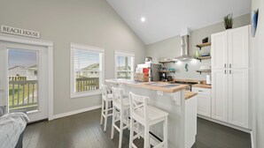A kitchen with a bar area, white cabinets, and a view of the backyard. - Brand New Home! Beach Views! Sleeps 6! Pets Welcome! (Bolivar Peninsula)