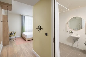 A modern hotel room with a bed, a desk, and a bathroom with a sink and mirror. - Hampton By Hilton London Old Street (London)