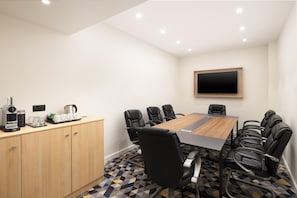 A conference room with a long table, black chairs, a coffee machine, and a TV on the wall. - Hampton By Hilton London Old Street (London)