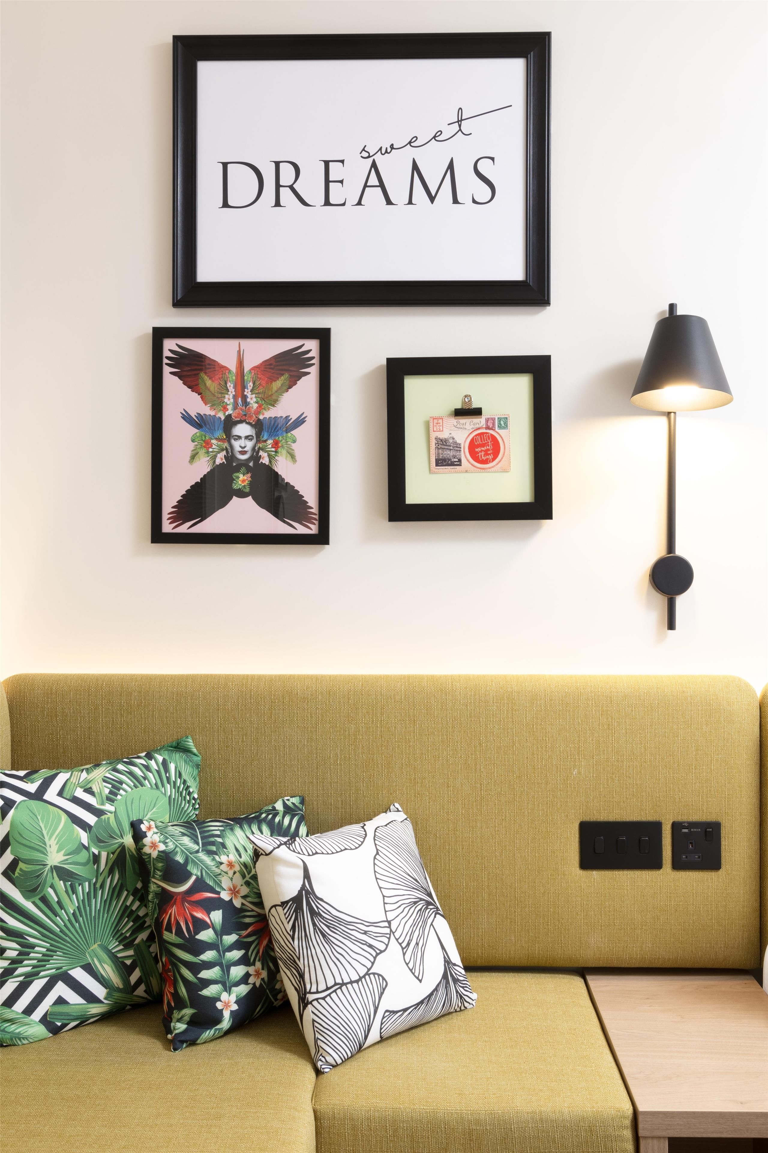 Una habitación con un sofá verde, una cita inspiradora enmarcada, una obra de arte de un pájaro decorativo, una postal antigua y una lámpara de pie moderna.