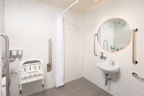A modern bathroom with a shower, a sink, and a wheelchair-accessible bench. - Hampton By Hilton London Old Street (London)
