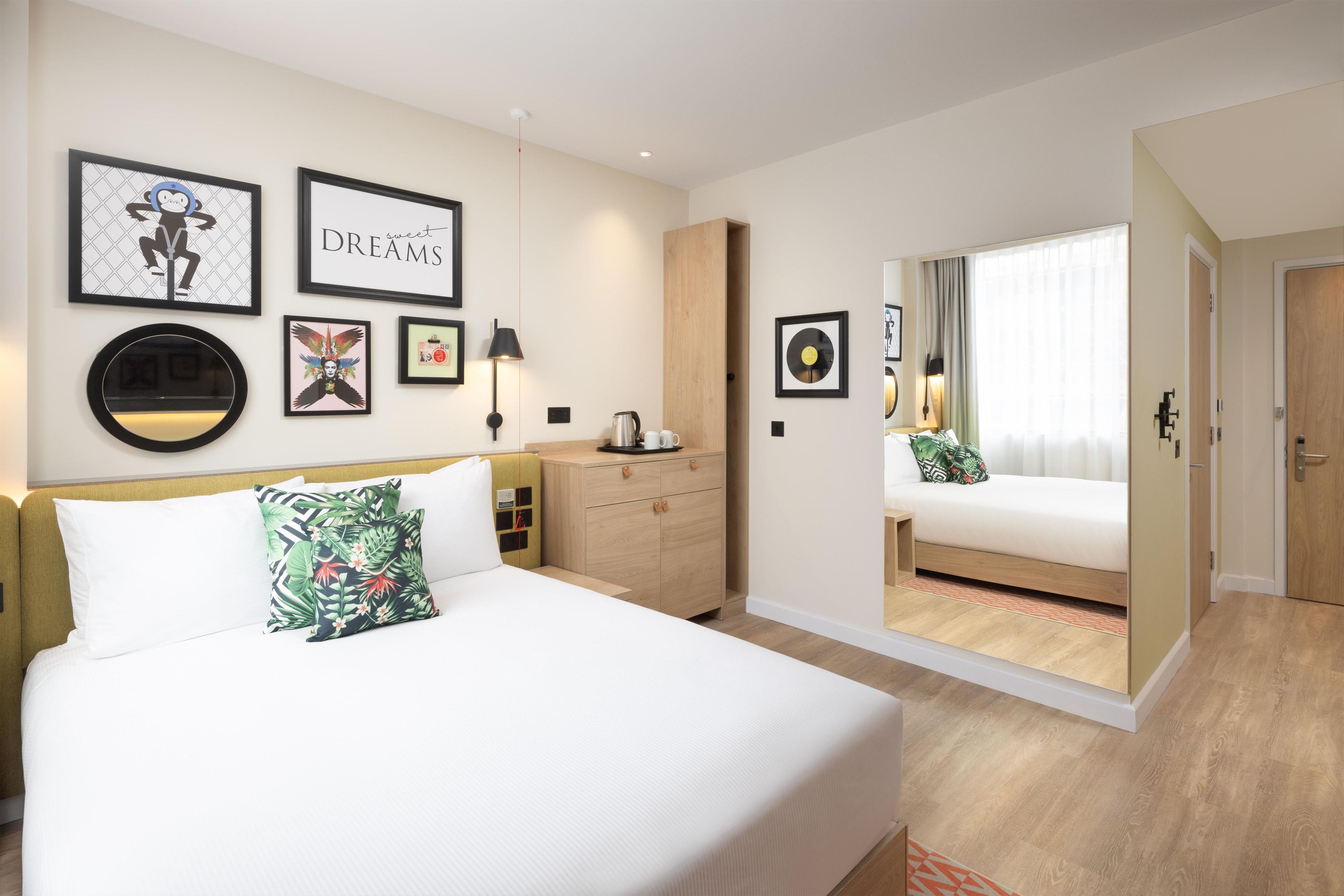 A hotel room with a bed, a nightstand, a dresser, and a door leading to another room.