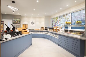 Um balcão de café da manhã moderno com design curvo, exibindo diversos alimentos e uma parede com saudações em vários idiomas.