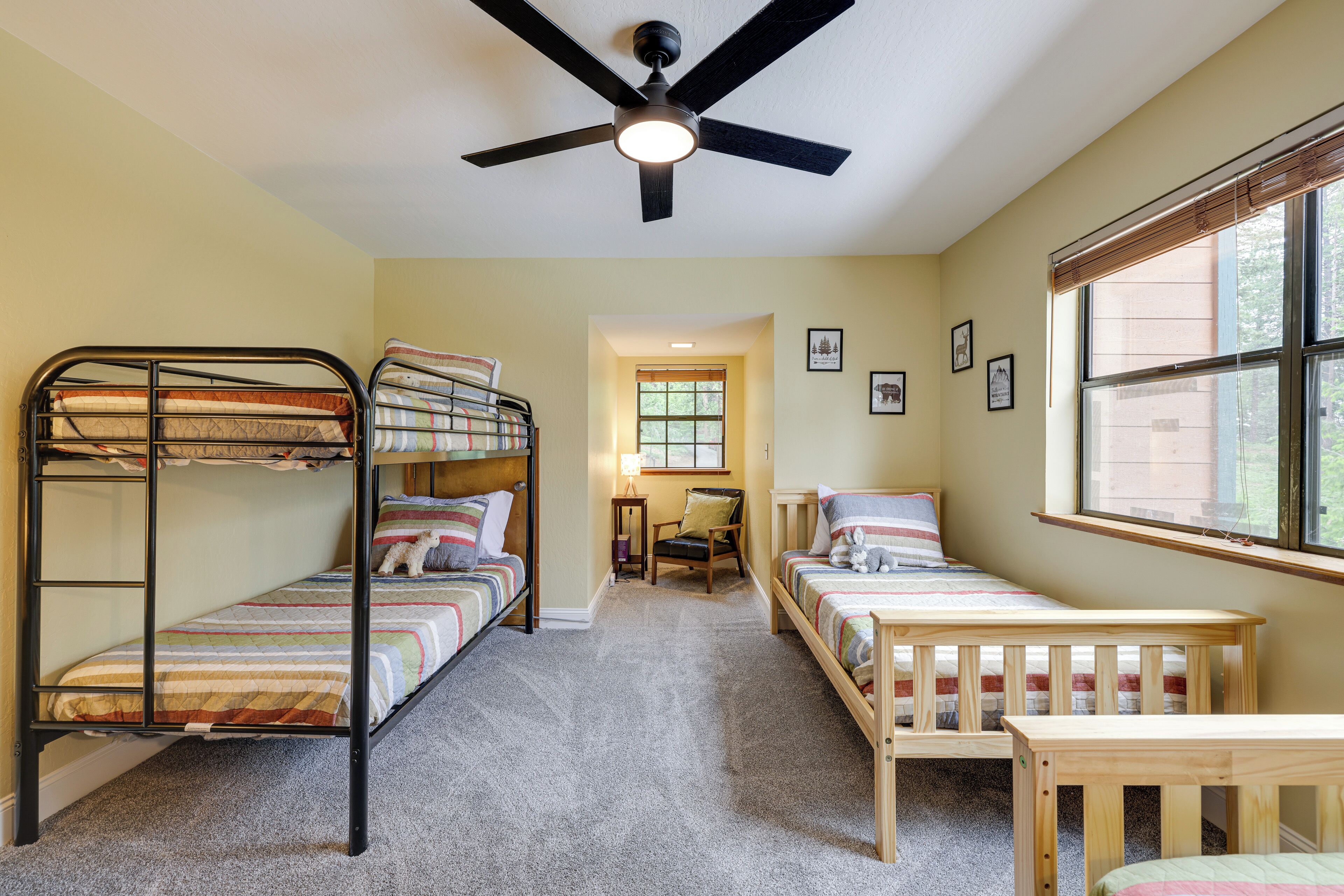 A room with bunk beds, a ceiling fan, a window with blinds, and a small table.
