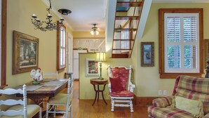 A dining area with a wooden table, white chairs, and a chandelier. There is a red chair and a plaid sofa in the living room. - Romantic Cottage in Washington Historic District (Washington)