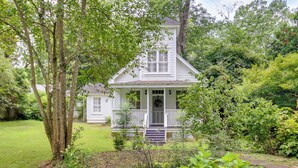 A white two-story house with a porch, surrounded by lush greenery and trees. - Romantic Cottage in Washington Historic District (Washington)