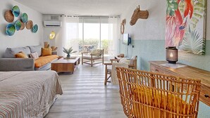 Un salón amplio con un ventanal grande, un sofá, una mesa de comedor y una silla de mimbre.