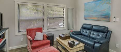 A living room with a red chair, a blue sofa, a wooden coffee table, and a painting on the wall.
