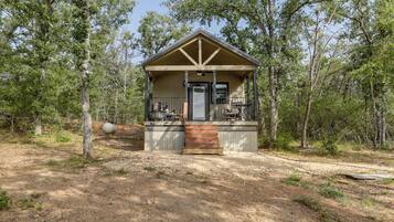 A small cabin with a porch, surrounded by trees.