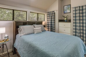 Ein Schlafzimmer mit einem Bett, einem Nachttisch, einer Lampe, einem Fenster und einer Kommode.