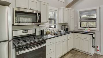 A modern kitchen with white cabinetry, a stainless steel stove, a microwave, and a sink.
