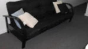 En sort sofa med to puder foran en ensfarvet væg.