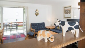 A living room with a blue sofa, a wooden coffee table, and two wooden animal figurines on a shelf. - Family basecamp for biking and skiing (Lenzerheide/Lai)