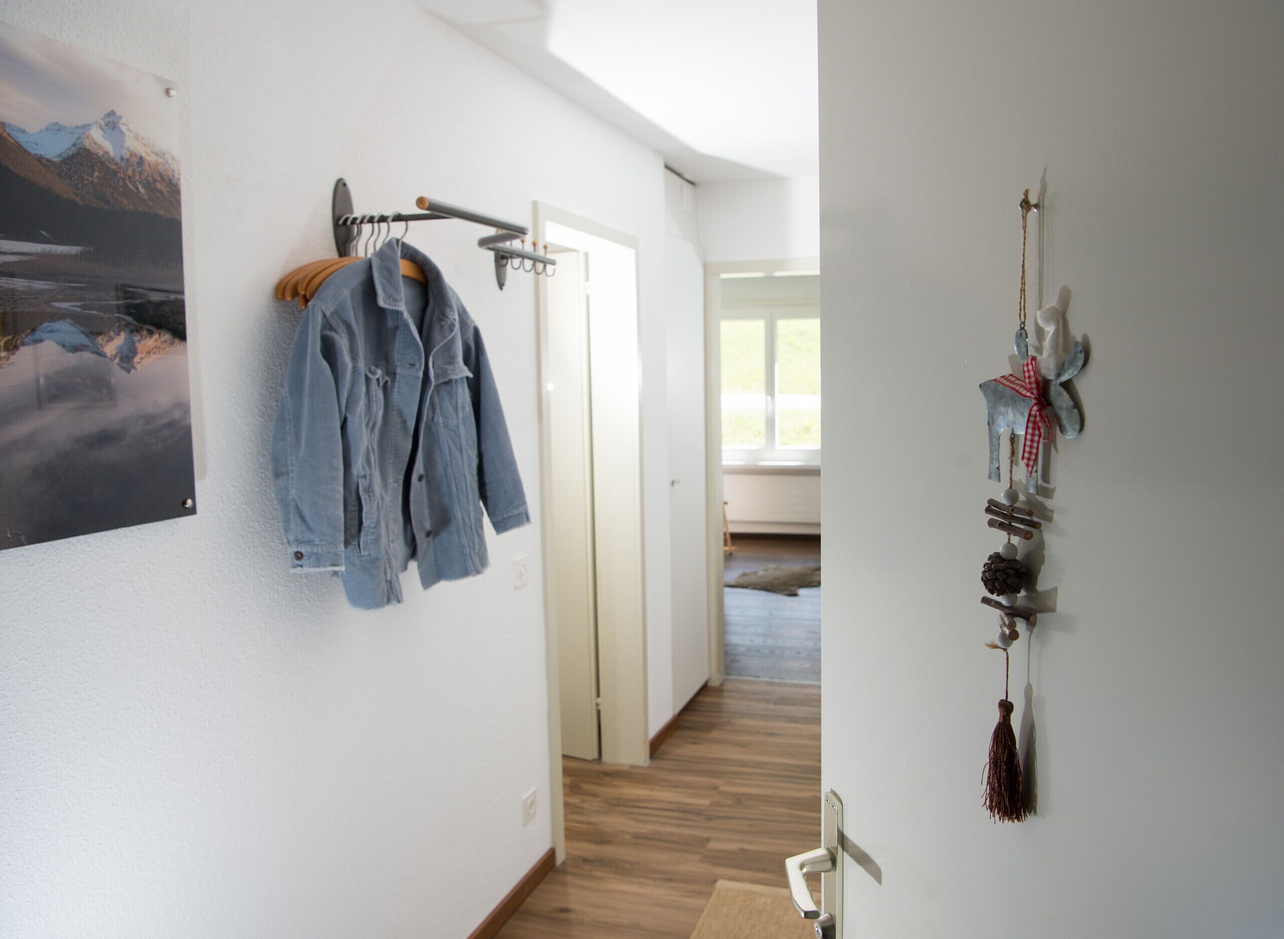 Un couloir avec un porte-manteau sur lequel est accrochée une veste en jean, un autre porte-manteau fixé au mur, et une décoration murale.
