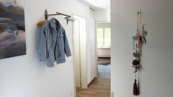 Un couloir avec un porte-manteau sur lequel est accrochée une veste en jean, un autre porte-manteau fixé au mur, et une décoration murale.