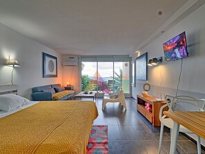 A modern hotel room with a bed, sofa, and a balcony with a view.