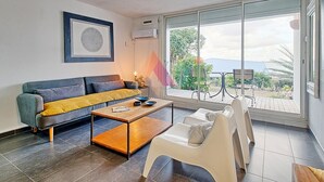 A modern living room with a sofa, coffee table, and a view of a garden through large sliding glass doors.
