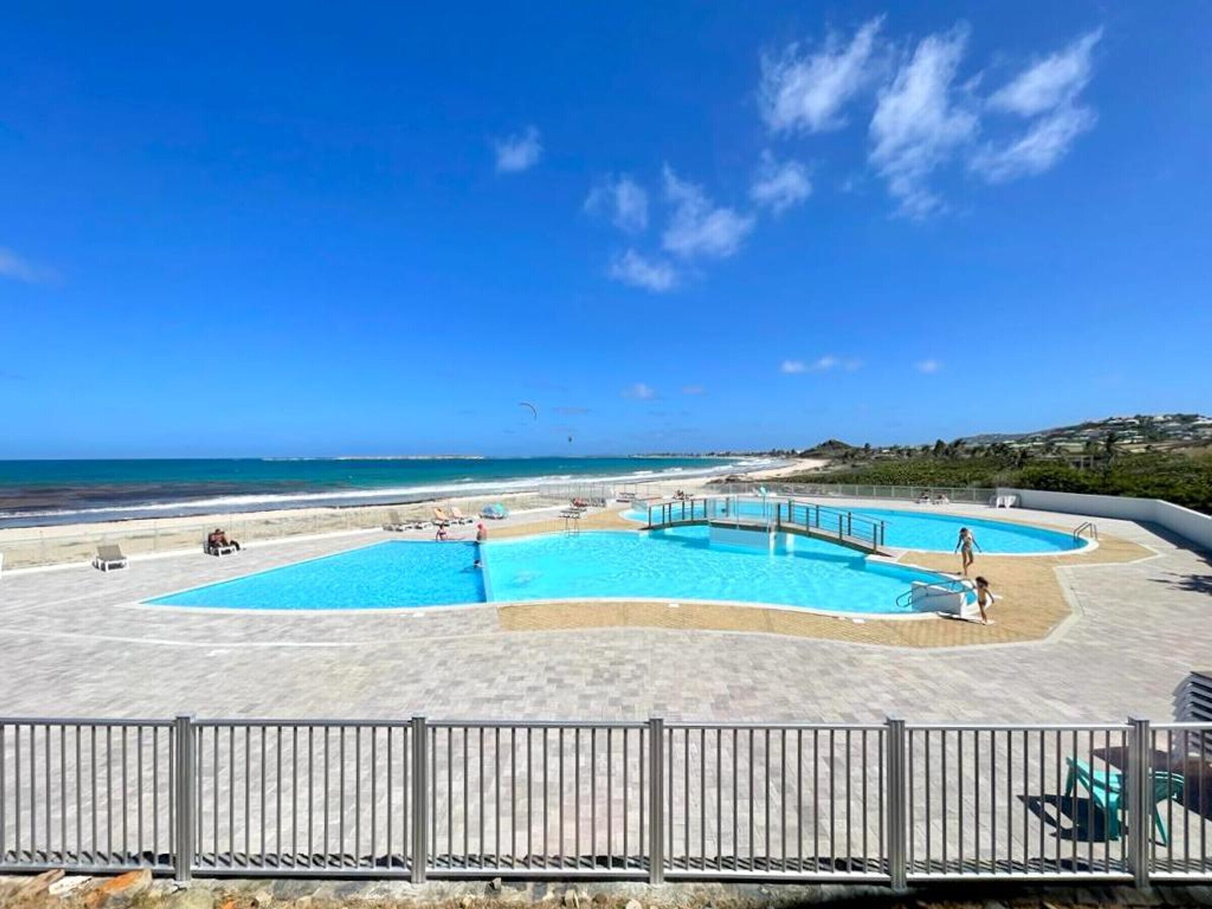 A pool area with multiple swimming pools, a beach, and a clear blue sky.