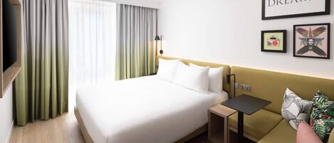 A hotel room with a bed, a small table, a sofa, and a TV.
