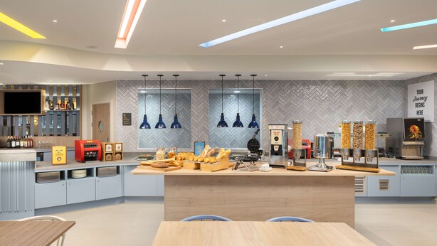 A modern kitchen with a central island, built-in appliances, and a variety of food items displayed. - Hampton By Hilton Rochdale (Rochdale)