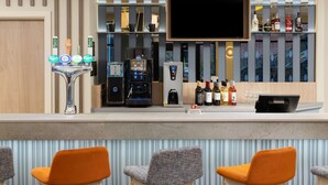 A bar area with a coffee machine, a TV mounted on the wall, and various bottles of alcohol. - Hampton By Hilton Rochdale (Rochdale)