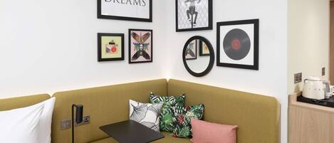 Een hoekappartement met een groene bank, een kleine tafel, een wandspiegel en kunstwerken, waaronder een vinylplaat en een bord met de tekst 'sweet DREAMS'.