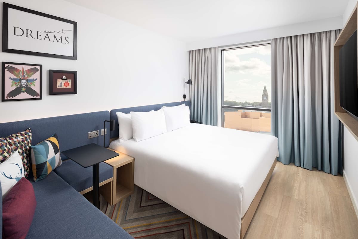 A hotel room with a bed, a small table, a sofa, and a window with curtains.