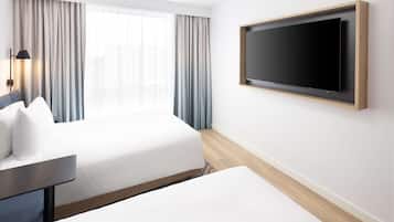 A hotel room with a bed, a desk, a TV mounted on the wall, and a window with curtains.