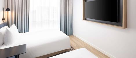 Habitación de hotel con cama, escritorio, televisor montado en la pared y ventana con cortinas.