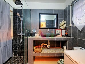 A bathroom with a shower, a sink with a mirror, a toilet, and a decorative vase. - Comfortable Studio in Grand Case near Beach (Saint-Martin)