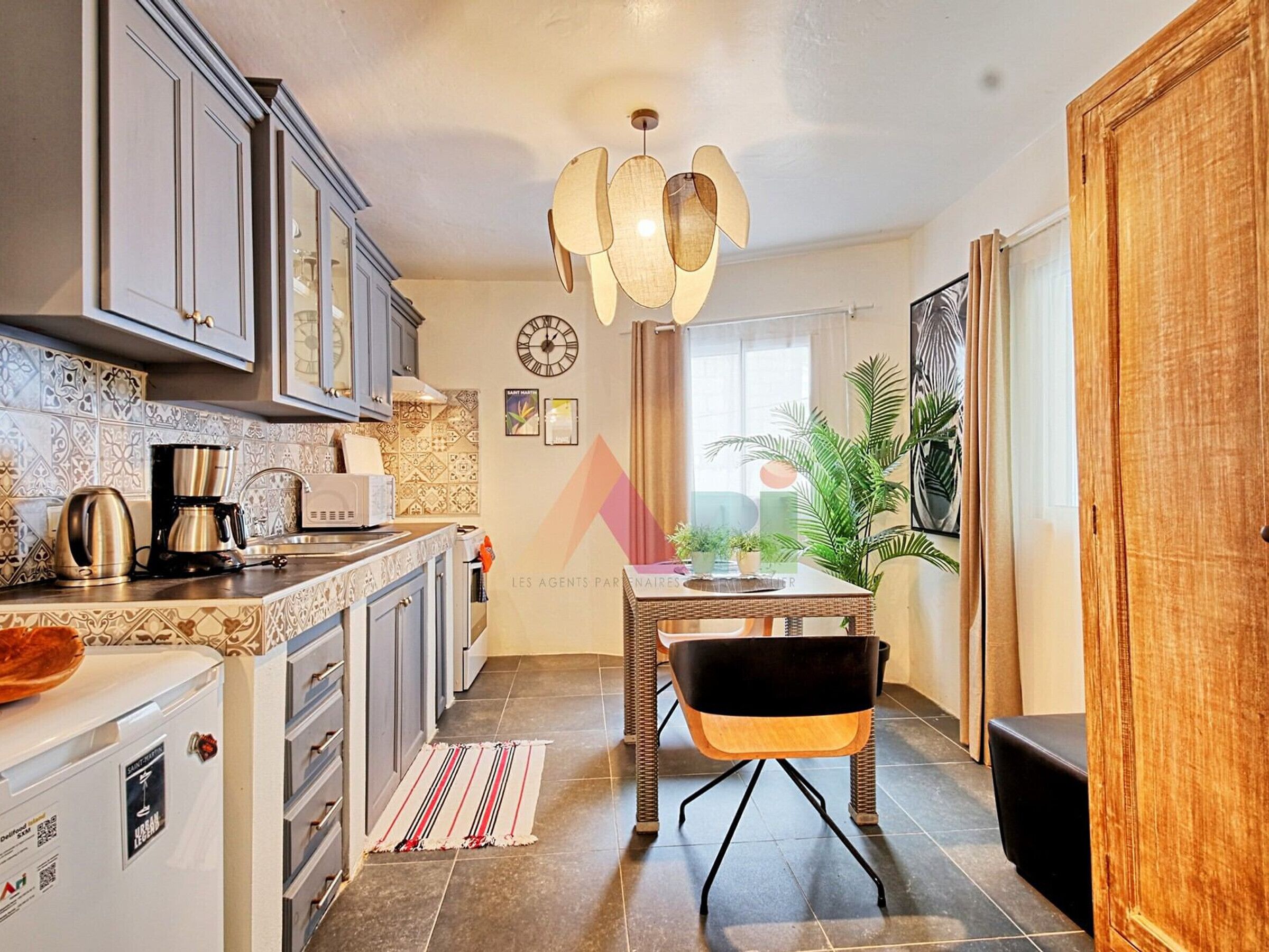 Ett modernt kök med matplats, utrustat med en kaffemaskin, en mikrovågsugn och ett kylskåp. Här finns ett matbord med stolar och en hängande lampa ovanför.