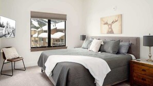 Une chambre avec un grand lit, une fenêtre donnant sur des immeubles, une chaise et une table de chevet.