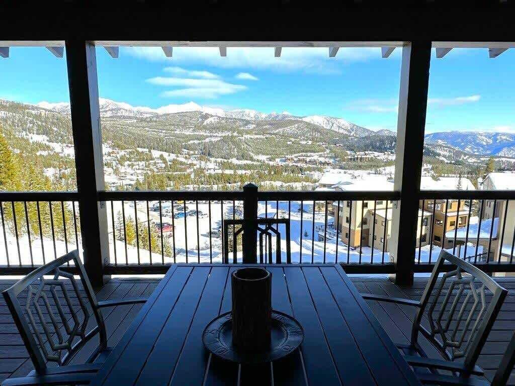 A covered outdoor seating area with a view of snow-covered mountains and a town below.