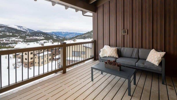 A balcony with a wooden floor, a gray sofa with white cushions, and a small table.