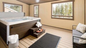 Une salle de spa équipée d’un bain à remous, d’un plancher en bois, d’un canapé et de grandes fenêtres donnant sur la forêt.