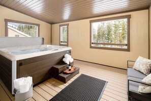 Une salle de spa équipée d’un bain à remous, d’un plancher en bois, d’un canapé et de grandes fenêtres donnant sur la forêt.