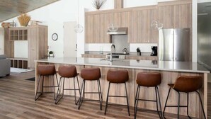 A modern kitchen with a central island, bar stools, wooden cabinets, and stainless steel appliances.