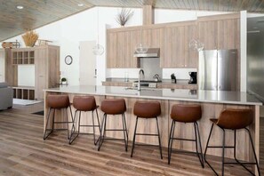 A modern kitchen with a central island, bar stools, wooden cabinets, and stainless steel appliances.