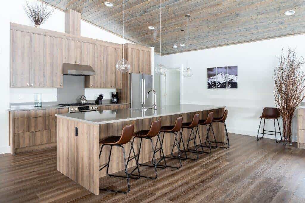 Una cocina moderna con armarios de madera, una isla grande con taburetes de bar, electrodomésticos de acero inoxidable e iluminación colgante.