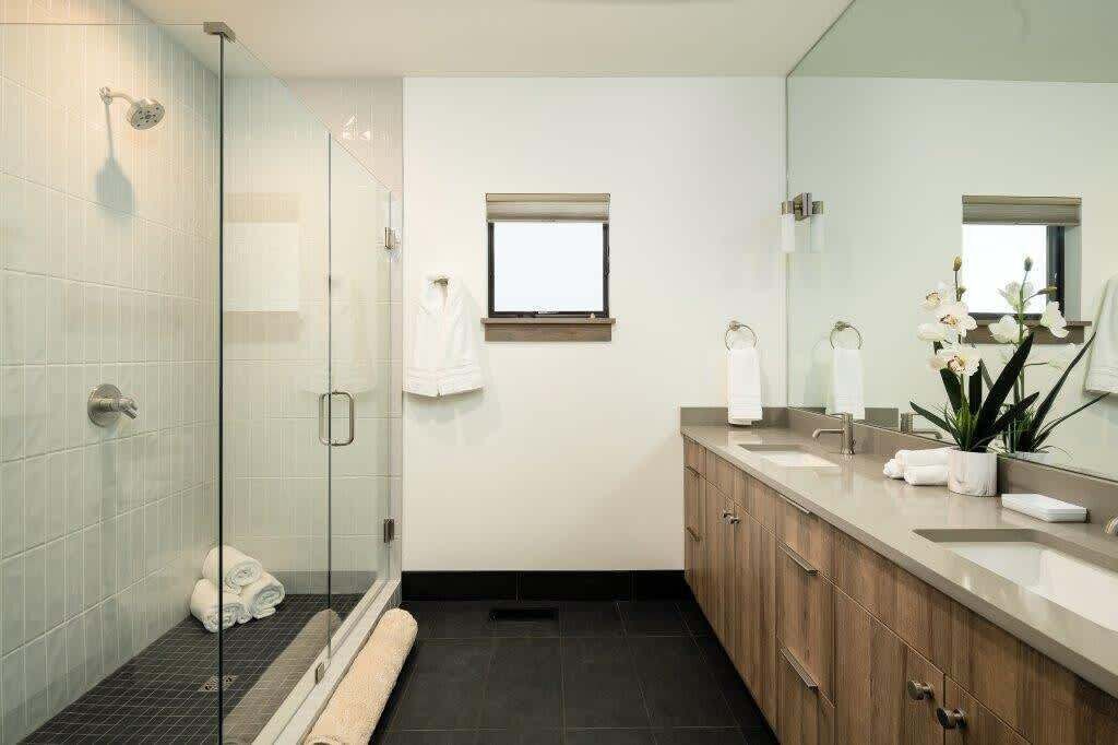 Een moderne badkamer met een glazen douchecabine, een grote spiegel en een houten wastafelmeubel met een wastafel.