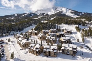 Une station de ski enneigée, avec plusieurs bâtiments de style chalet, un télésiège et un paysage montagneux en toile de fond.
