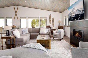 A spacious living room with a large sectional sofa, a fireplace, and a mountain painting on the wall.