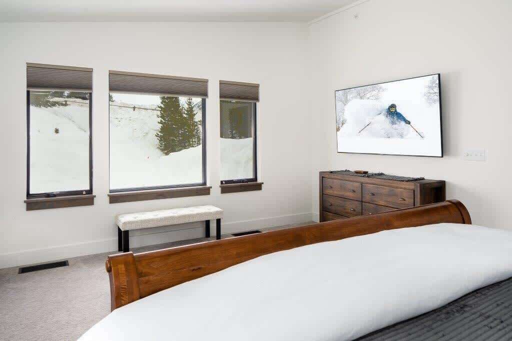 Een slaapkamer met een bed, een bankje, een dressoir en drie ramen met uitzicht op sneeuw.