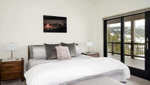 Une chambre à coucher avec un grand lit, deux tables de chevet, une commode, une fenêtre donnant sur un paysage enneigé et un tableau encadré au mur.