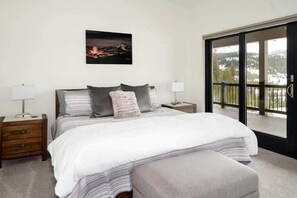 A bedroom with a large bed, two bedside tables, a nightstand, a window with a view of a snowy landscape, and a framed picture on the wall.