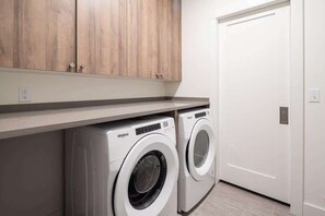 A laundry area with two front-loading washers, wooden cabinets above, and a white door.