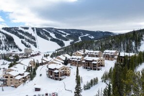 A snow-covered resort with multiple buildings, a ski slope, and a mountainous backdrop.
